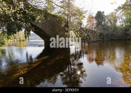 Ancient stone arch bridge over a river in Fort Augustus, Scottish Highlands, with woodland reflections in the peaty water. Stock Photo