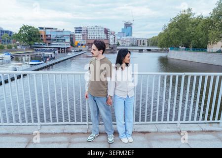 Full length of young interracial couple holding hands on city bridge Stock Photo