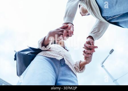 Low angle view of interracial couple holding hands against bright sky in the city Stock Photo
