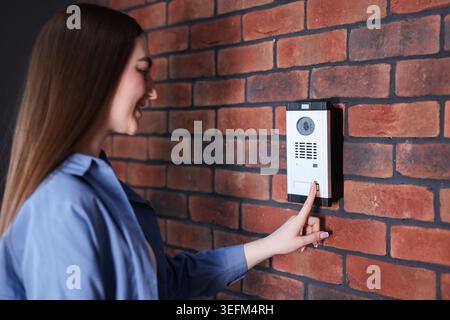 Woman pressing button on intercom panel near brick wall Stock Photo