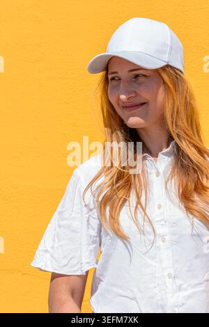 Young woman with red hair wearing white baseball cap smiling Stock Photo