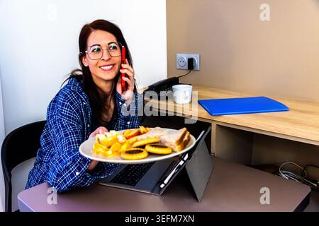 Woman multitasking working remotely having breakfast and talking on phone Stock Photo