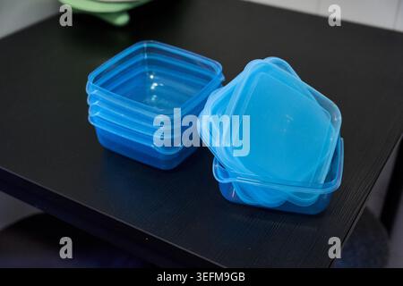 A set of small blue plastic food storage containers with lids stacked separately on a dark table Stock Photo