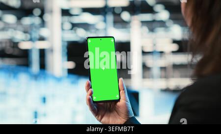 Chroma key smartphone used by data center admin to troubleshoot rigs issues. Woman in server hub using isolated screen mobile phone to analyze system logs, fixing equipment computer bugs Stock Photo
