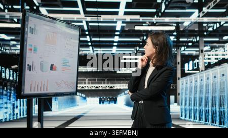 Data center manager looking at infrastructure status infographics on monitor. Server farm employee analyzing AR simulation and audit charts on display to oversee equipment Stock Photo