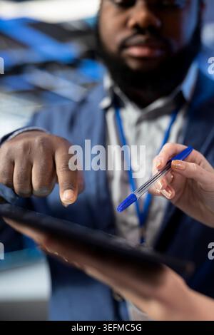 Cooperating, tablet closeup and team of engineers in data center brainstorming to protect against network threats. Audit systems, computer bugs, and cybersecurity teamworking coworkers in server farm Stock Photo