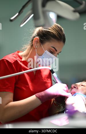 Female Dental Hygienist Wearing Mask and Gloves Performing Dental Cleaning on Patient in Clinic Stock Photo