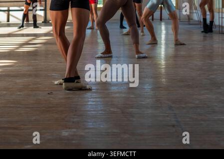 A group of dancers practices in a dance studio in Cuba. The low-angle shot focuses on muscular legs and worn-out slippers resting on an old, polished Stock Photo