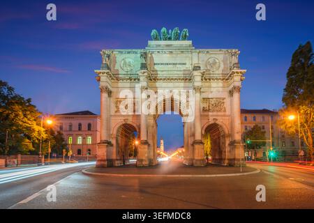 Dramatic twilight view of the Siegestor monument in Munich, Bavaria, Germany, featuring vibrant light trails from passing cars. Stock Photo