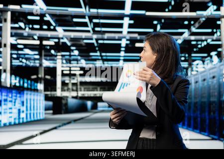 Data center female engineer auditing documentation papers, doing infrastructure management. Server room worker analyzes technical documents for accuracy, planning disaster recovery protocols Stock Photo