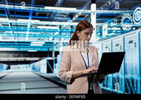 Data center engineer managing infrastructure systems for uptime and efficiency using laptop. Server room IT professional upgrading enterprise networks hardware using notebook Stock Photo