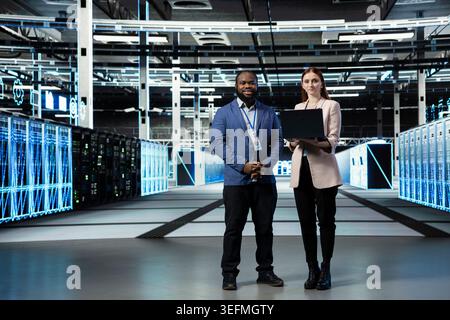 Portrait of smiling data center engineering team working together to install and upgrade server racks systems. Happy server room teamworking colleagues monitor automated IT infrastructure performance Stock Photo