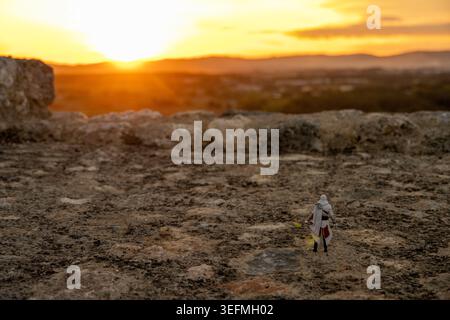 Monteriggioni, Italy - 16 Sep 24: Small hooded action figure stands on a stone wall in Monteriggioni, Tuscany, Italy, with a soft-focus sunset over ro Stock Photo