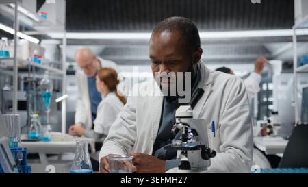Assay development specialist pipetting reactant into blue solution for purity analysis. Man in research facility lab adding liquid agent to test tube to observe chemical reaction properties, camera A Stock Photo