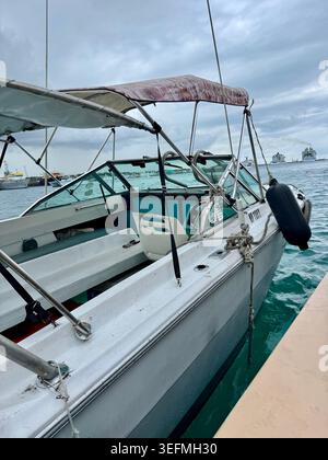 Close-up view of a white motorboat or speed boat docked at a pier in the turquoise waters of Nassau, Bahamas, under an overcast sky. Stock Photo
