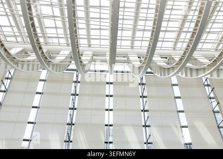 Looking up at modern glass roof with white steel ribs, sun flare, geometric lines, minimal architectural interior background. Stock Photo