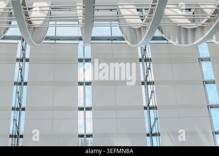 Modern glass atrium interior with white curved ceiling panels, skylight, and large window wall, bright minimal architectural background. Stock Photo