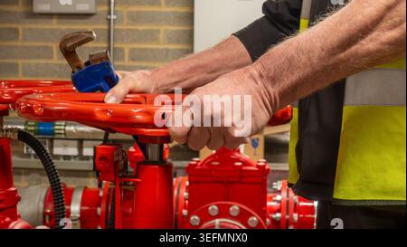 Sprinkler system service engineer operating a red flow valve with a wrench in his hand. Wet fire safety sprinkler system being maintained by a special Stock Photo