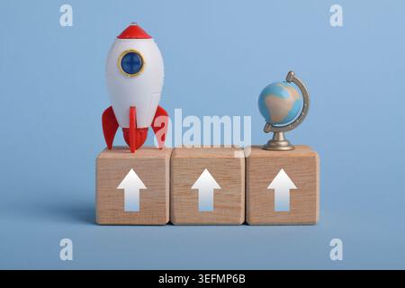 Upward arrows on wooden blocks with rocket and globe. Symbolizing business growth, rising success, global expansion, progress, and upward trend concep Stock Photo