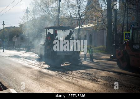 Workers laying fresh asphalt on main city street, heavy machinery helping at work to pave road. Stock Photo