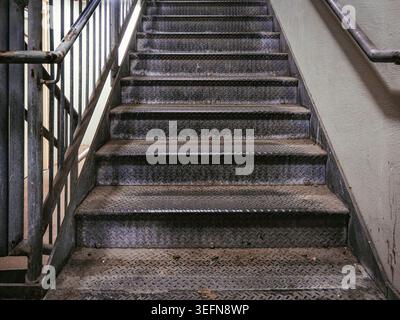 Industrial diamond plate metal stairs with steel handrails leading upward inside a gritty urban building or public transit station structure Stock Photo