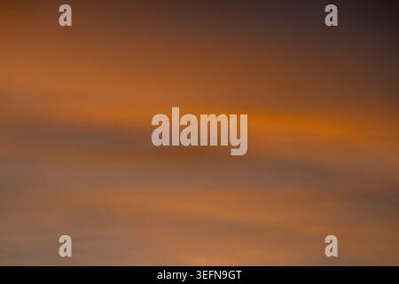 Soft defocused sky with warm orange and amber tones blending through layered cloud bands in an abstract gradient Stock Photo