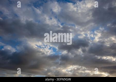Mixed cloud formations with bright white cumulus and dark grey masses against vivid blue sky creating strong contrast Stock Photo