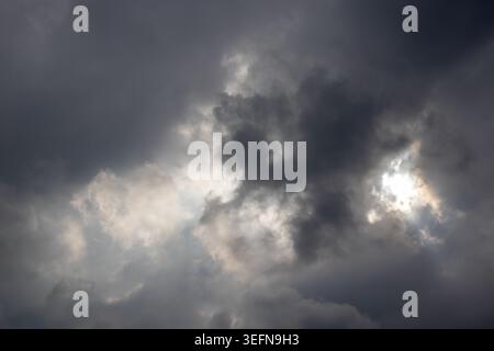 Sun partially obscured by dark storm clouds with warm light edging through creating dramatic contrast across turbulent sky Stock Photo
