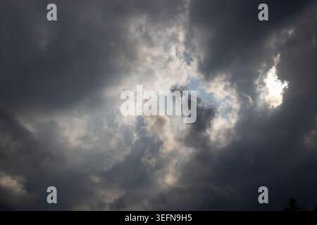 Storm clouds parting to reveal blue sky with sun breaking through creating dramatic light and dark contrasts Stock Photo
