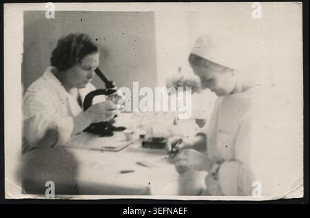 Women in a medical laboratory examining samples with a microscope in Russia, 1950s. Authentic Soviet photograph. Stock Photo