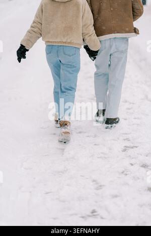 Two individuals tread snowcovered ground in warm winter attire. Lively companions enjoying frosty outdoor walk in denim and shearling jackets Stock Photo