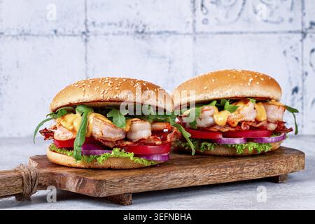 Two shrimp burgers and buns with sesame seeds, bacon, lettuce, tomatoes and onions, On a wooden board Stock Photo