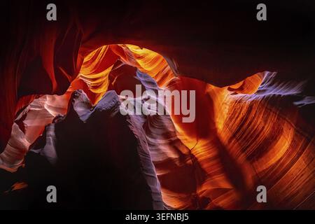Slot canyon walls showing sunlit sandstone formations with vibrant orange, red, and purple hues creating a natural abstract underground landscape in a Stock Photo