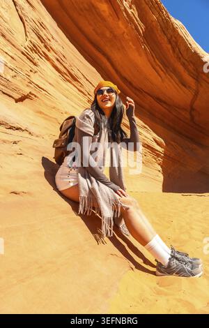 Woman traveler sitting in the desert sandstone formation of biidi the arch cave, enjoying her outdoor adventure and travel experience in page, arizona Stock Photo