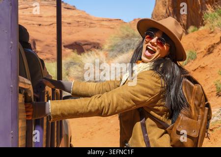 Young woman smiling and expressing surprise while riding a navajo jeep tour, exploring the red desert landscape of monument valley during an adventure Stock Photo