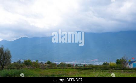 Sunbeams breaking through dramatic clouds above rural villages at the foot of Cangshan Mountain in Dali, Yunnan, China, creating a striking crepuscula Stock Photo