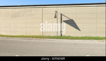 Concrete wall with a strip of grass and a street sign with its shadow on the wall. Empty road in front. Background for copy space. Stock Photo