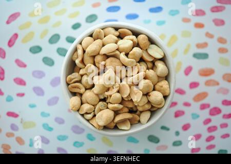 Snack bowl filled with roasted peanuts on colored background Stock Photo