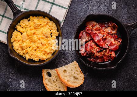 Cooked scrambled eggs and fried bacon in portion pans, top view. Stock Photo