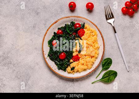 Cooked omelette and spinach with tomatoes on a light background, top view. Stock Photo