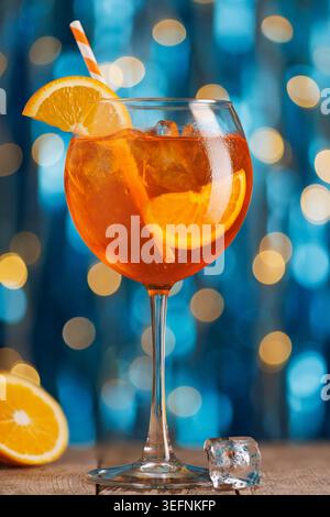 Aperol spritz cocktail with ice, orange slice garnish and striped straw on wooden table bright blue bokeh background Stock Photo