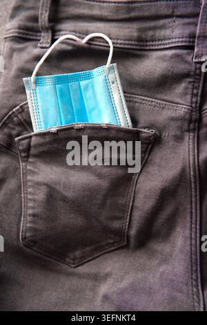 A medical disposable mask, neatly folded in the back pocket of dark jeans. Vertical photo Stock Photo