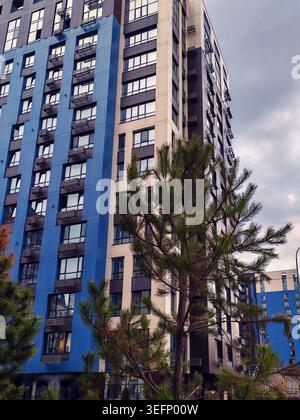 Modern apartment facades rise above landscaped shrubs, combining brick cladding, light stone panels, dark windows and metal fencing. The image fits Stock Photo