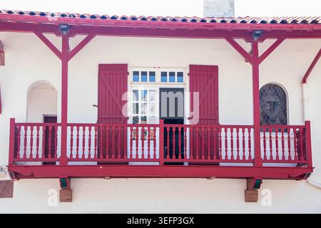 Bidart, France - August 15, 2025: A close-up view of a traditional whitewashed house facade featuring an iconic red wooden balcony with decorated rail Stock Photo