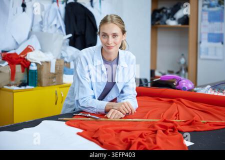 Innovative woman clothing designer engaged in fabric selection surrounded by sewing tools Stock Photo