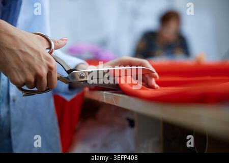 Focused artisan carefully measuring and cutting red textile on wooden workspace Stock Photo