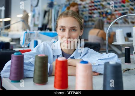 Craftswoman surrounded by colorful threads and machines. Stock Photo
