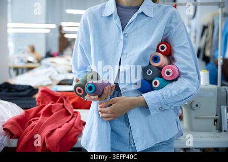 Woman organizing thread spools carefully, brightly colored yarns in industrial sewing environment Stock Photo