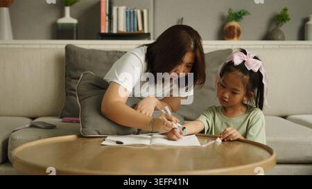 Mother helping child drawing in notebook, learning and bonding at home Stock Photo