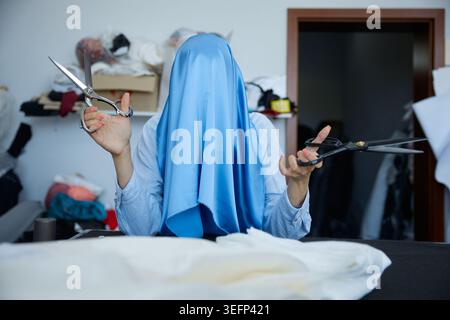 Individual dressed in blue holding scissors over textile materials in studio Stock Photo